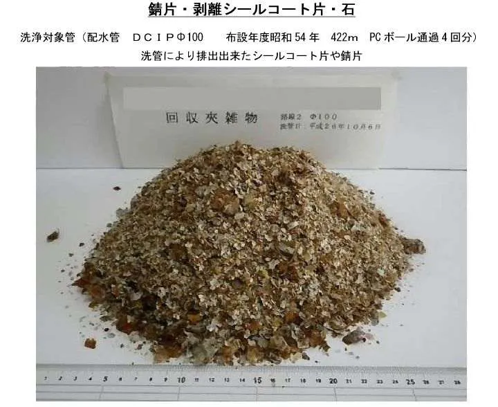 洗管により排出された錆片とシールコート片が、目盛りのある台の上に山状に積まれている写真
