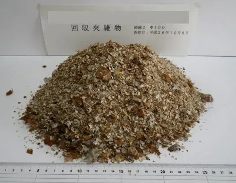 洗管で排出された砂状の夾雑物が、目盛りのある台の上に山状に積まれている写真